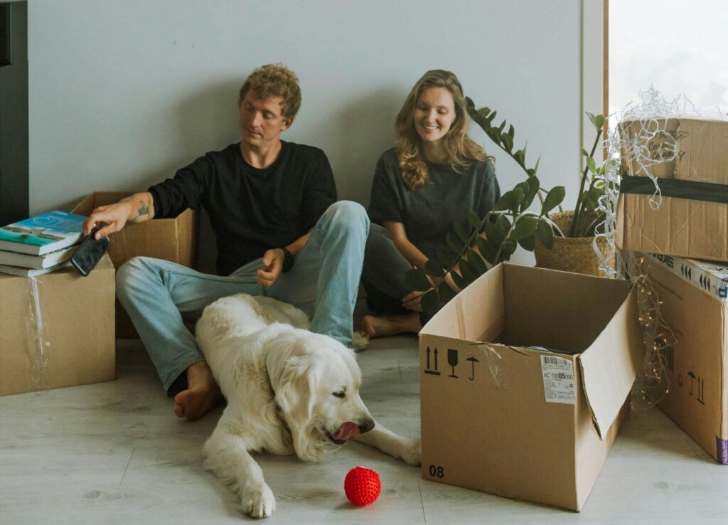 A couple sitting with their dog and unpacked boxes in a new home.
