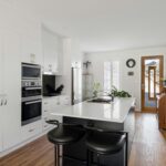 A sleek contemporary kitchen featuring a modern island, white cabinets, and wooden flooring.