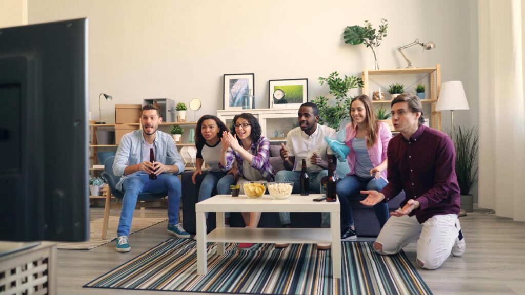 A diverse group of adults cheering and watching a sports event together in a cozy living room.
