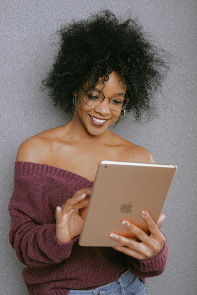 A young woman with curly hair smiling while using a tablet indoors.