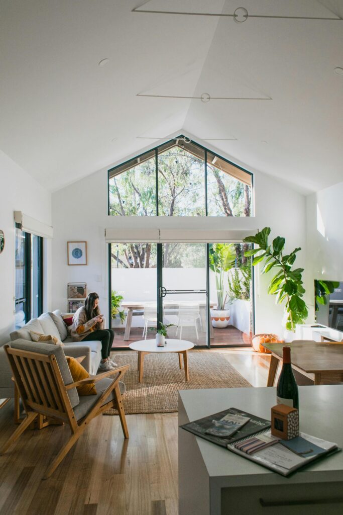 Distant woman sitting in couch in spacious contemporary living room with armchair near side table and glass wall at home