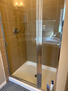 Glass-shower enclosure with sliding doors, brown tiled walls, and a bottle on the shower floor nearby.
