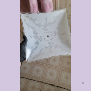 Decorative white square ceiling medallion with ornate scrollwork, held by a gloved hand.