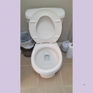 White porcelain toilet with the seat up in a bathroom, placed between a trash can and a toilet brush station.