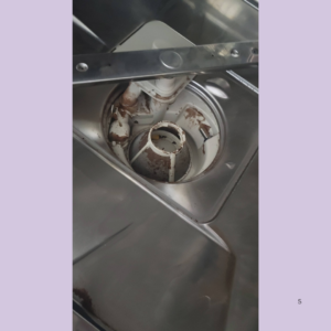 Rusty, corroded inner mechanism of a stainless steel appliance, with exposed pipes and circular housing