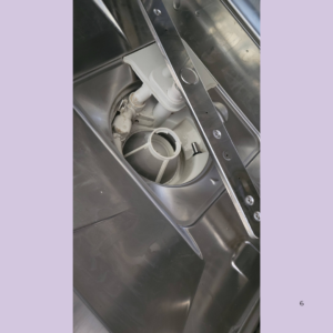 Close-up of a stainless steel appliance interior showing a white plastic drain pump and circular filter housing inside a dishwasher or similar unit.