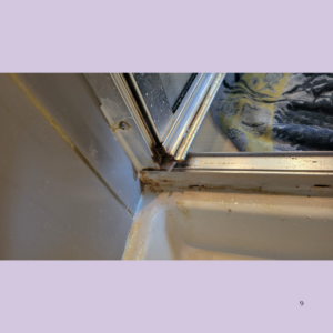 Rusty, dirty shower door track with grime along the bottom of a sliding glass door in a bathroom.