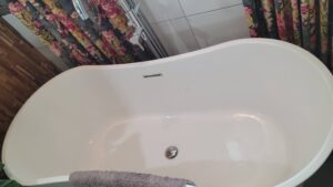 White freestanding oval bathtub with a chrome faucet, gray towel draped on the edge, and floral curtains in the background.