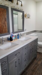 Double-sink bathroom vanity with gray cabinets, white countertop, and a geometric mosaic backsplash under two mirrors.