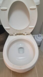 White toilet with the lid up and seat exposed, showing dirt and stains on the rim and seat edge in a bathroom.
