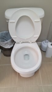 Open-lid white toilet in a bathroom with a trash can and toilet brush nearby.