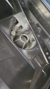 Open access area inside a front-loading washing machine showing the drum opening and white filter housing/plumbing components.