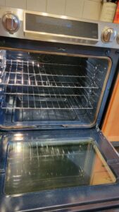 Open oven door revealing empty oven cavity with two metal racks and a dark interior. The stainless steel exterior and control dials are visible.