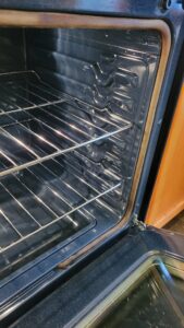 Empty oven interior with two wire racks and the door open, exposing a dark cavity.