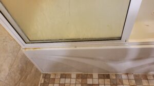 Dirty glass shower door with grime along the bottom frame and rust on the tub edge.