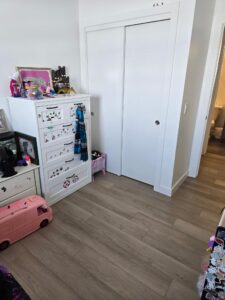 Corner of a child’s bedroom featuring a white dresser with stickers, a pink toy bus on the floor, and a large white sliding-door closet behind.