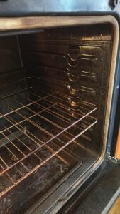 Interior view of a dirty oven with metal racks and dark grime on walls and bottom